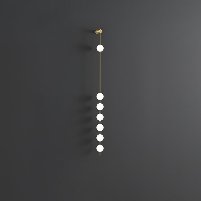 The Clérachic Stacked Globe Wall Sconce in brass, lit, six globes glowing against a dark grey backdrop.