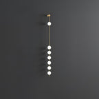 The Clérachic Stacked Globe Wall Sconce in brass, lit, six globes glowing against a dark grey backdrop.