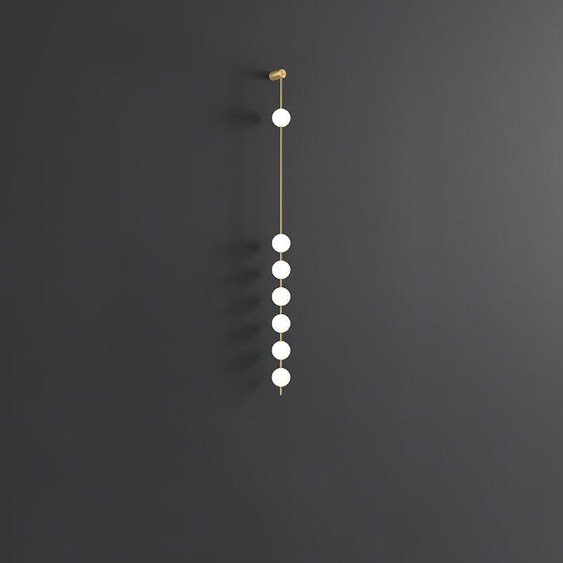 The Clérachic Stacked Globe Wall Sconce in brass, lit, six globes shown at an angle on a dark grey backdrop.