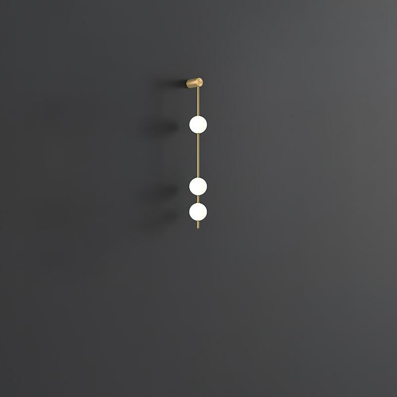 The Clérachic Stacked Globe Wall Sconce in brass, lit, three globes glowing against a dark grey backdrop.