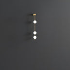 The Clérachic Stacked Globe Wall Sconce in brass, lit, three globes glowing against a dark grey backdrop.