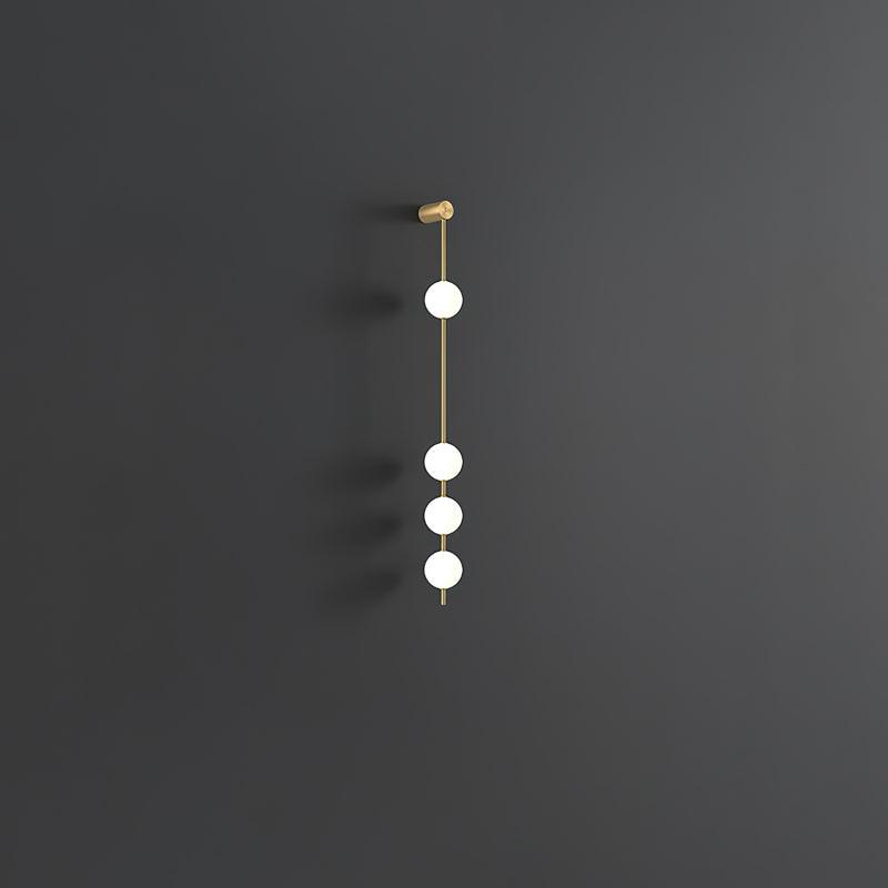 The Clérachic Stacked Globe Wall Sconce in brass, lit, four globes glowing against a dark grey backdrop.