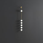 The Clérachic Stacked Globe Wall Sconce in brass, lit, six globes shown at an angle against dark grey.