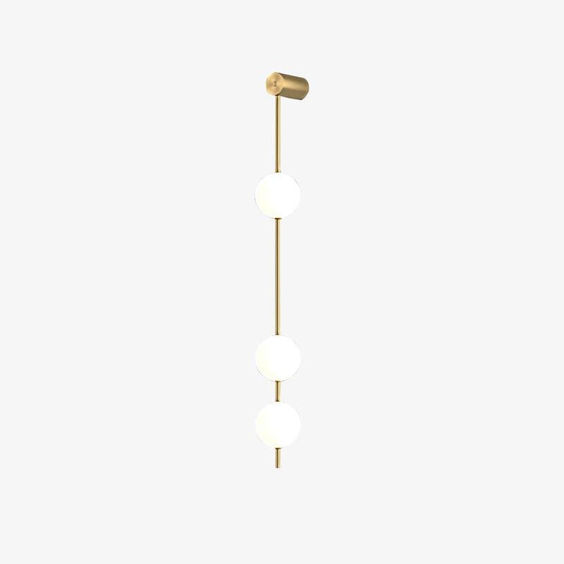 The Clérachic Stacked Globe Wall Sconce in brass, lit, three globes centred on a plain white backdrop.