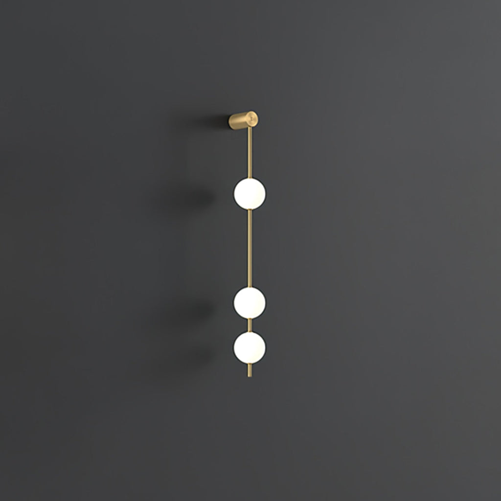 The Clérachic Stacked Globe Wall Sconce in brass, lit, three globes glowing softly on a dark grey backdrop.