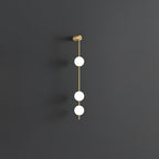 The Clérachic Stacked Globe Wall Sconce in brass, lit, three globes glowing softly on a dark grey backdrop.
