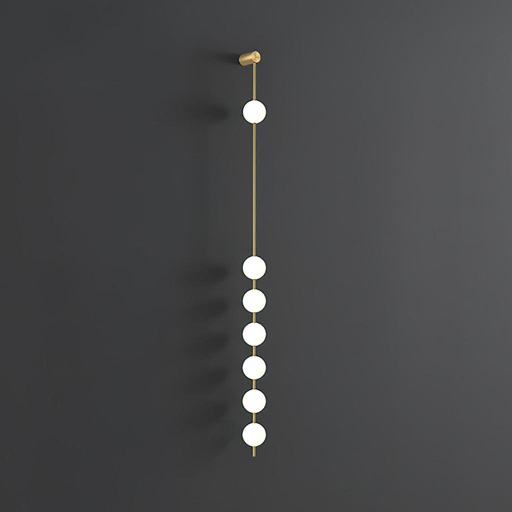 The Clérachic Stacked Globe Wall Sconce in brass, lit, six globes glowing down a dark grey backdrop.