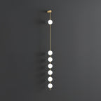 The Clérachic Stacked Globe Wall Sconce in brass, lit, six globes glowing down a dark grey backdrop.