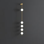 The Clérachic Stacked Globe Wall Sconce in brass, lit, five globes glowing against a dark grey backdrop.