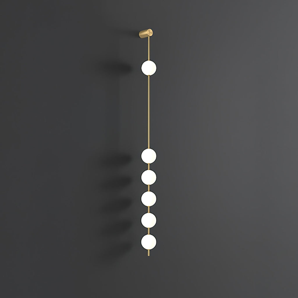 The Clérachic Stacked Globe Wall Sconce in brass, lit, six globes glowing the full drop on dark grey.