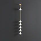 The Clérachic Stacked Globe Wall Sconce in brass, lit, six globes glowing the full drop on dark grey.