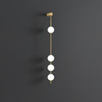 The Clérachic Stacked Globe Wall Sconce in brass, lit, five globes glowing against a dark grey studio wall.