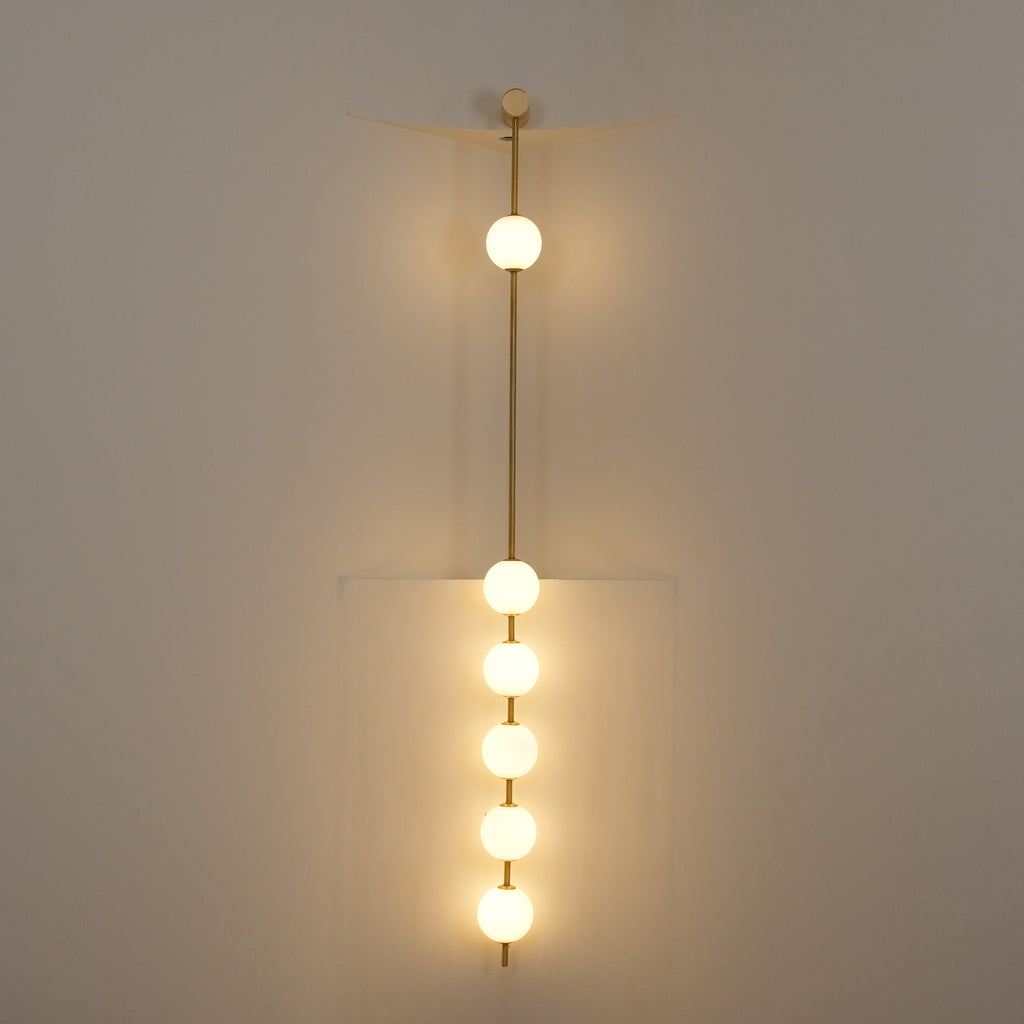 The Clérachic Stacked Globe Wall Sconce in brass, lit, five globes glowing dimly in a stairwell corner.
