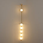 The Clérachic Stacked Globe Wall Sconce in brass, lit, five globes glowing dimly in a stairwell corner.