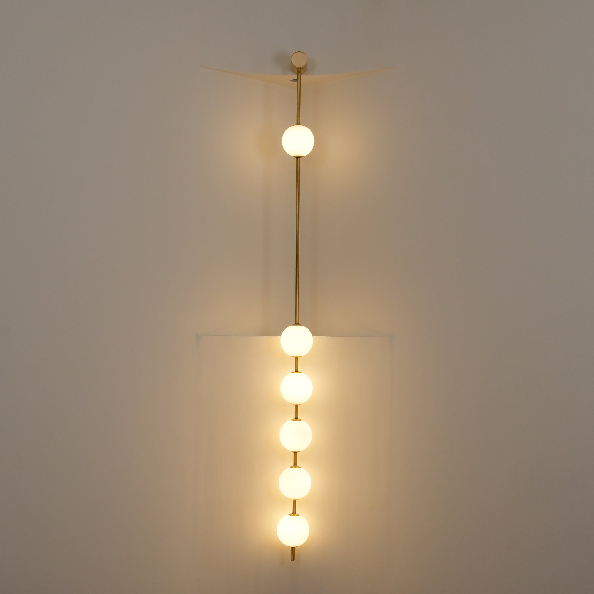 The Clérachic Stacked Globe Wall Sconce in brass, lit, five globes glowing dimly in a stairwell corner.