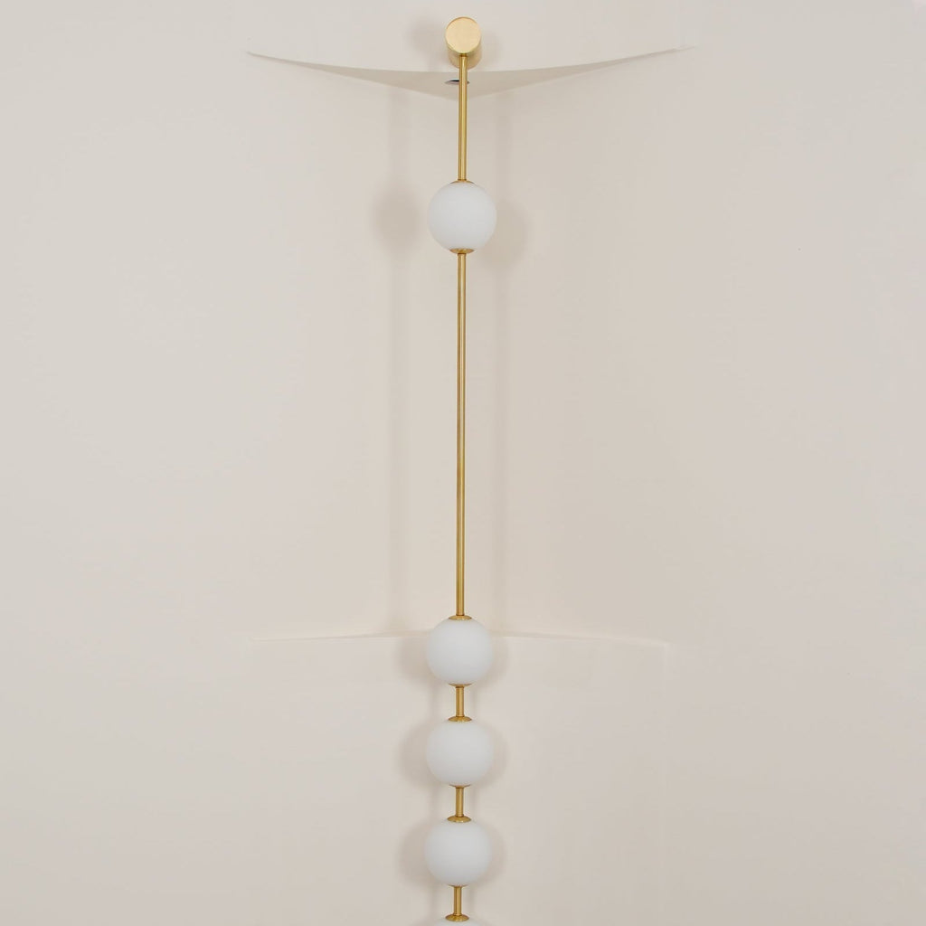 The Clérachic Stacked Globe Wall Sconce in brass, lit, four globes glowing in a cream-walled stairwell corner.
