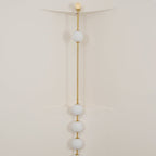 The Clérachic Stacked Globe Wall Sconce in brass, lit, four globes glowing in a cream-walled stairwell corner.