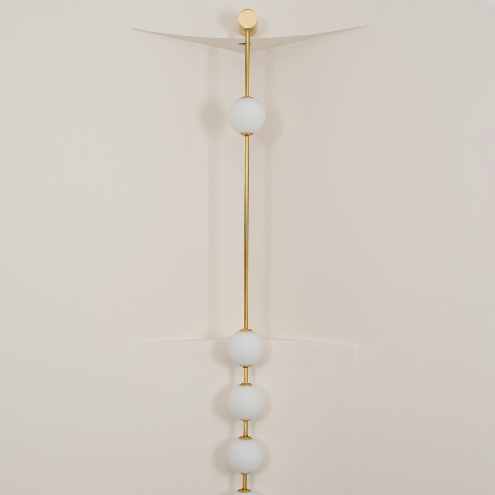 The Clérachic Stacked Globe Wall Sconce in brass, lit, four globes glowing in a cream-walled stairwell corner.