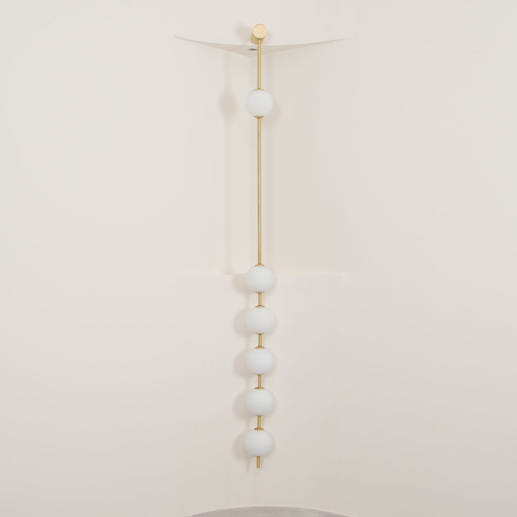 The Clérachic Stacked Globe Wall Sconce in brass, lit, six globes glowing in a cream-walled stairwell corner.