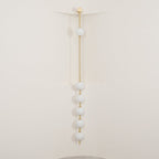 The Clérachic Stacked Globe Wall Sconce in brass, lit, six globes glowing in a cream-walled stairwell corner.