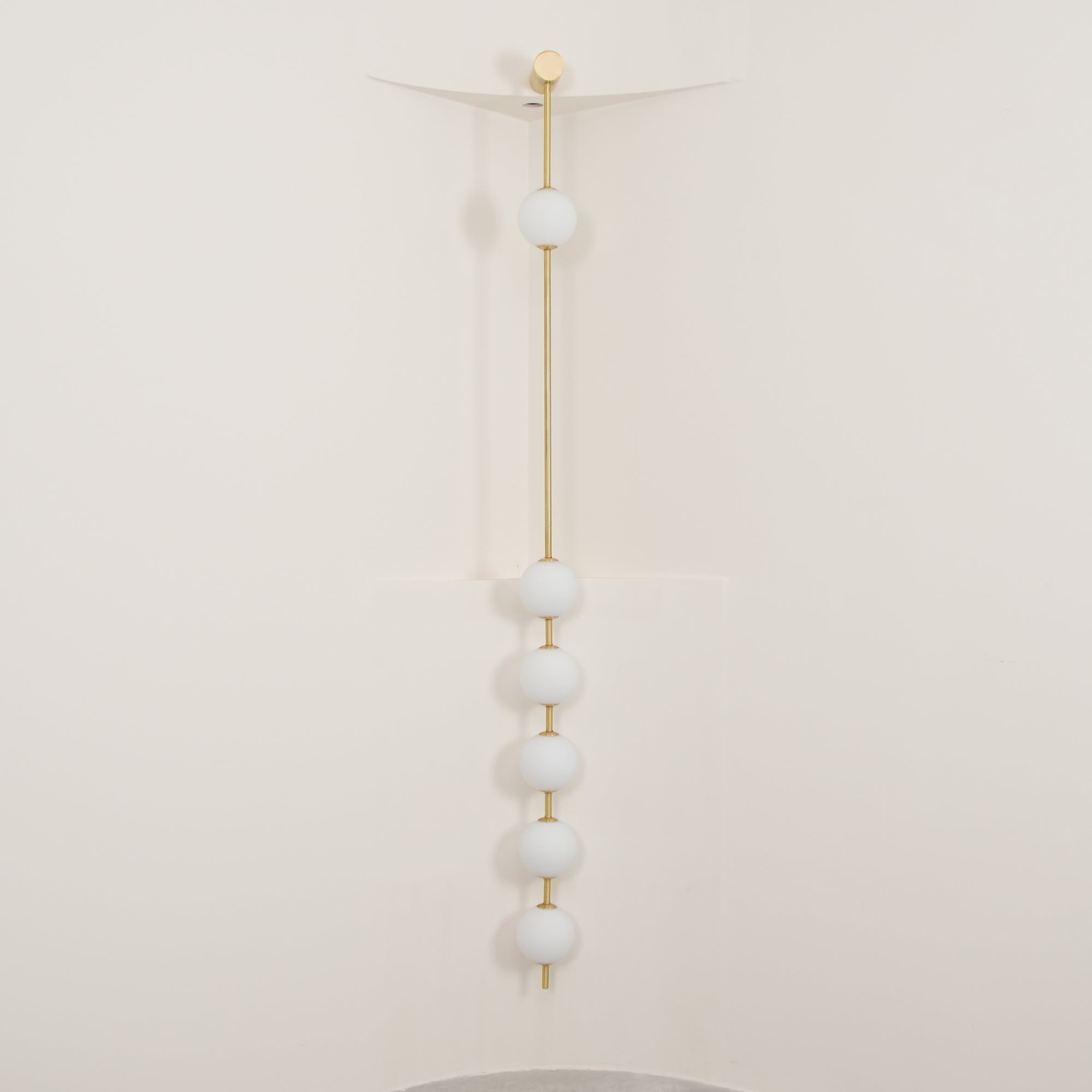 The Clérachic Stacked Globe Wall Sconce in brass, lit, six globes glowing in a cream-walled stairwell corner.
