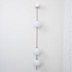 The Clérachic Stacked Globe Wall Sconce in brushed nickel, lit, three globes beside a sheer lace curtain.