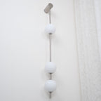 The Clérachic Stacked Globe Wall Sconce in brushed nickel, lit, three globes shown close to a lace curtain.