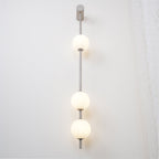 The Clérachic Stacked Globe Wall Sconce in brushed nickel, lit, four globes glowing beside a curtained window.