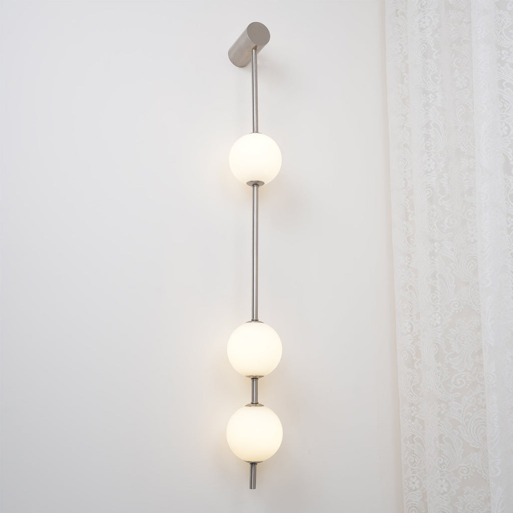 The Clérachic Stacked Globe Wall Sconce in brushed nickel, lit, four globes photographed beside sheer lace.