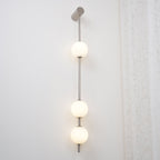 The Clérachic Stacked Globe Wall Sconce in brushed nickel, lit, four globes photographed beside sheer lace.