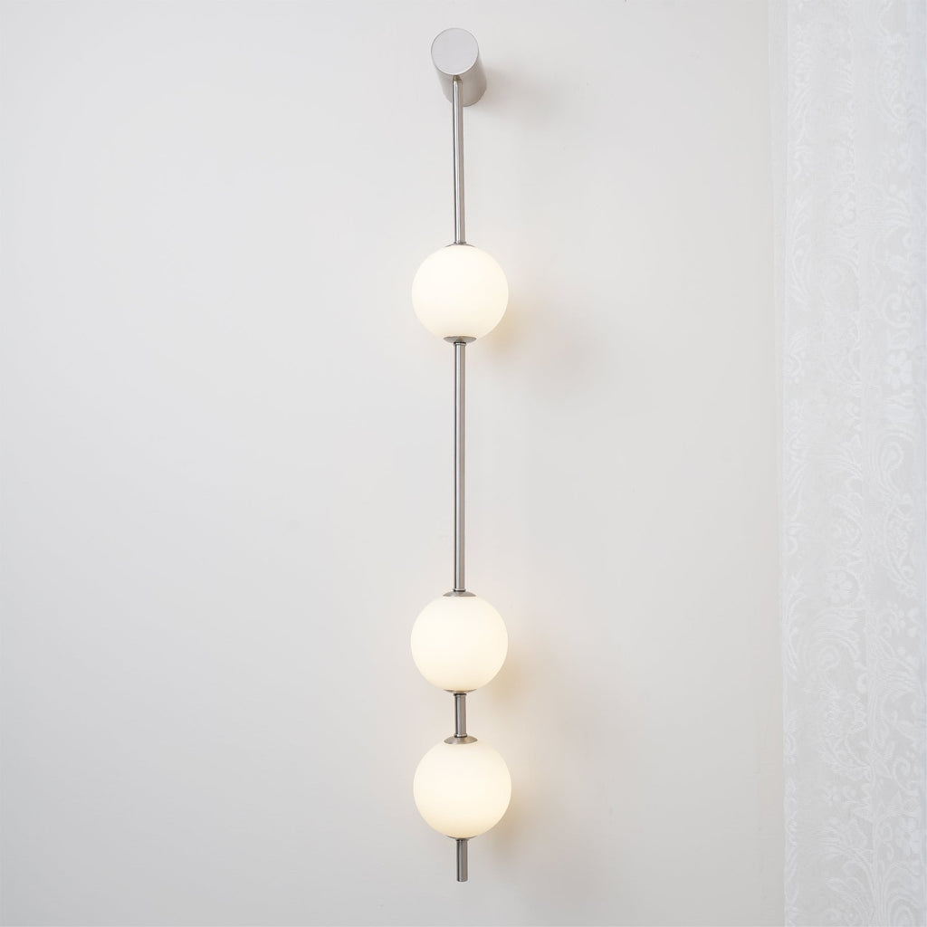 The Clérachic Stacked Globe Wall Sconce in brushed nickel, lit, three globes glowing against a plain wall.