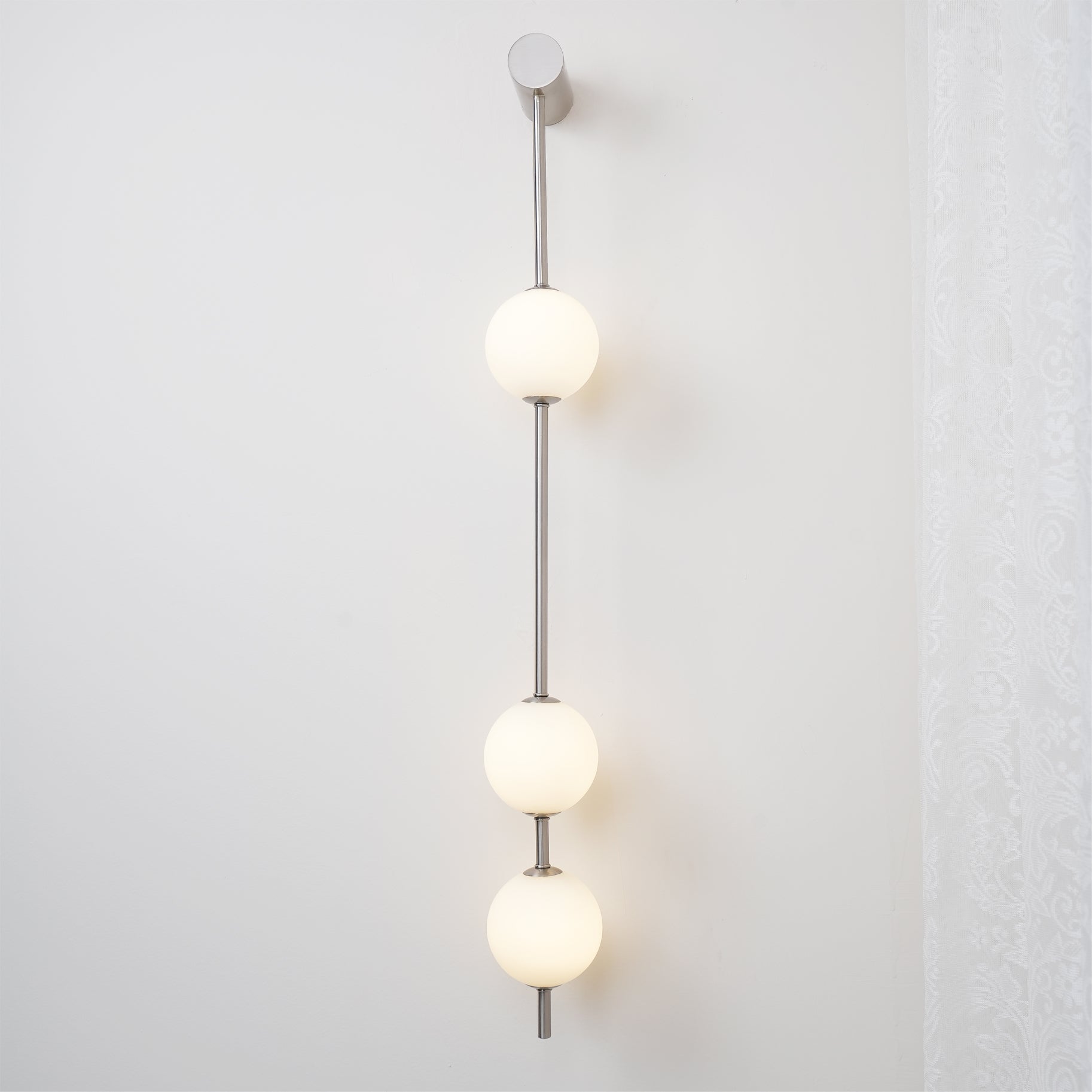 The Clérachic Stacked Globe Wall Sconce in brushed nickel, lit, three globes glowing against a plain wall.