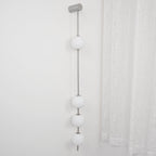 The Clérachic Stacked Globe Wall Sconce in brushed nickel, lit, five globes beside a sheer lace curtain.