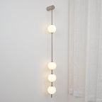 The Clérachic Stacked Globe Wall Sconce in brushed nickel, lit, four globes shown close to a curtained window.