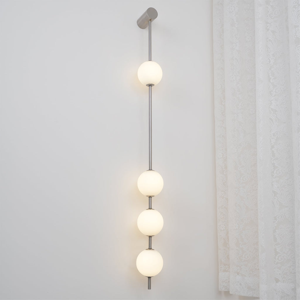 The Clérachic Stacked Globe Wall Sconce in brushed nickel, lit, five globes glowing beside a curtained window.