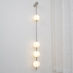 The Clérachic Stacked Globe Wall Sconce in brushed nickel, lit, five globes glowing beside a curtained window.