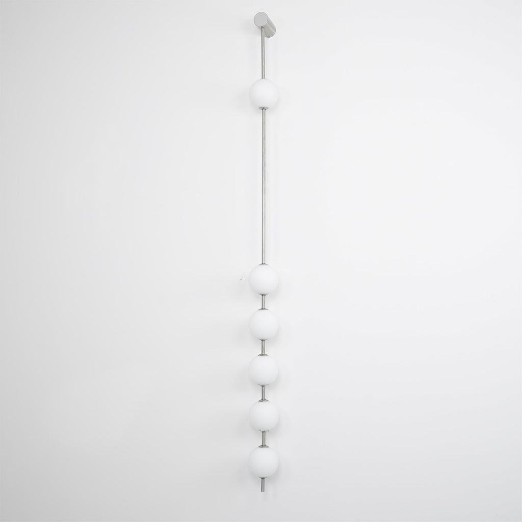 The Clérachic Stacked Globe Wall Sconce in brushed nickel, lit, four globes photographed near sheer lace.