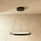 One black ring pendant from Clérachic hangs low on thin cables, framed by a soft sand-toned wall and ceiling.