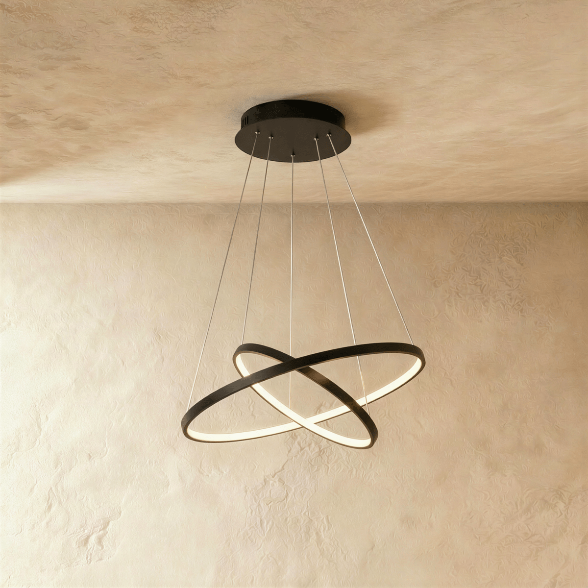 Two black rings cross at an angle in this Clérachic pendant, each edge glowing warm against a plaster wall.