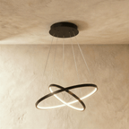 Clérachic's black two-ring chandelier shows its rings overlapping in an X, lit warm above a textured room.