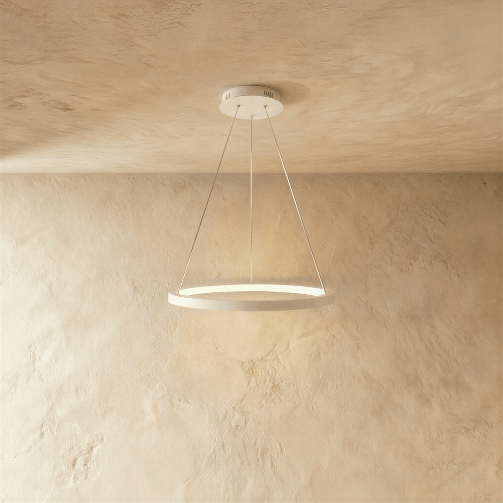 Clérachic's single-ring pendant in white hangs from three fine cables against a warm plaster wall.
