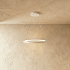 Clérachic's single-ring pendant in white hangs from three fine cables against a warm plaster wall.