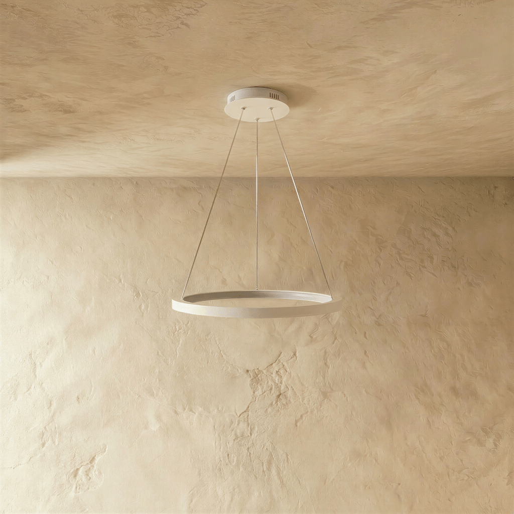 A white ring pendant by Clérachic glows softly on slender cables below a stone-textured ceiling.