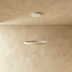 A white ring pendant by Clérachic glows softly on slender cables below a stone-textured ceiling.