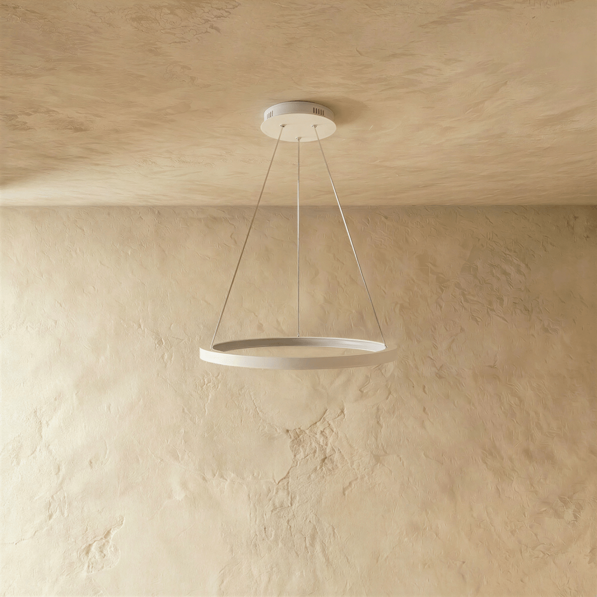 A white ring pendant by Clérachic glows softly on slender cables below a stone-textured ceiling.
