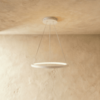 Clérachic's white ring pendant floats gently, its LED edge glowing warm against a pale plaster backdrop.