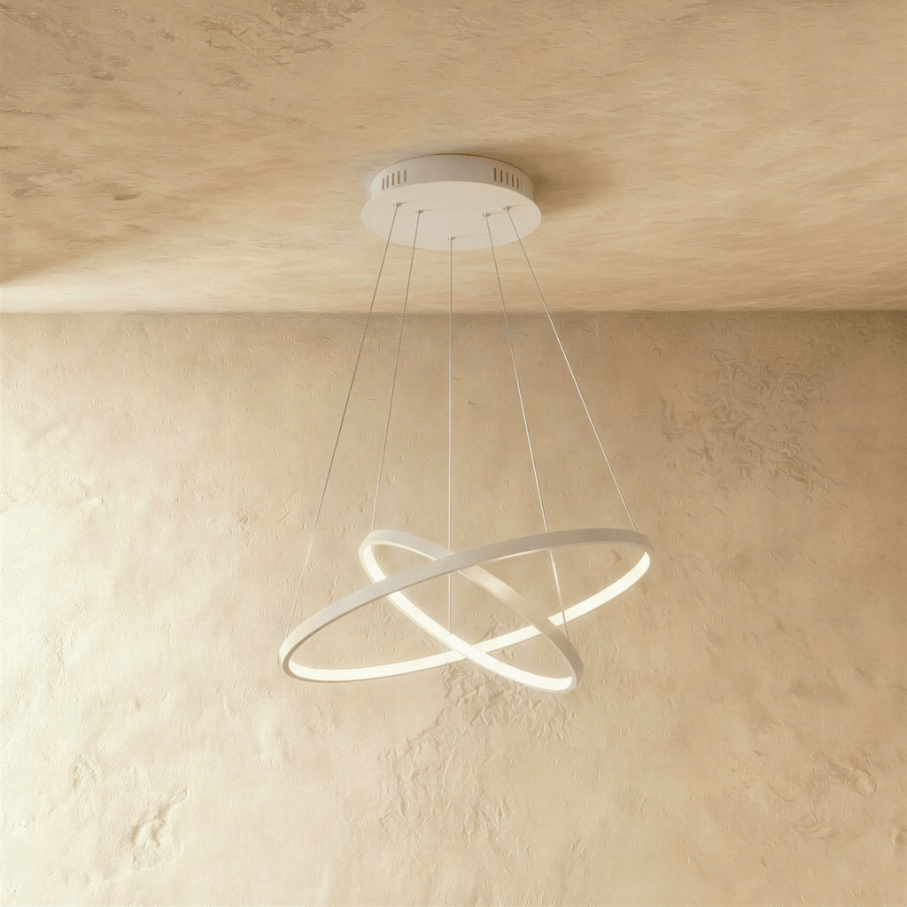 Two white rings cross at an angle in this Clérachic pendant, each edge glowing warm against a plaster wall.