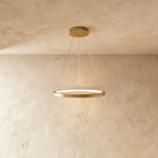 Clérachic's single-ring pendant in a golden finish hangs from three fine cables against a plaster wall.