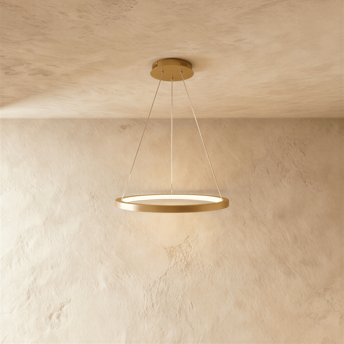 Clérachic's single-ring pendant in a golden finish hangs from three fine cables against a plaster wall.