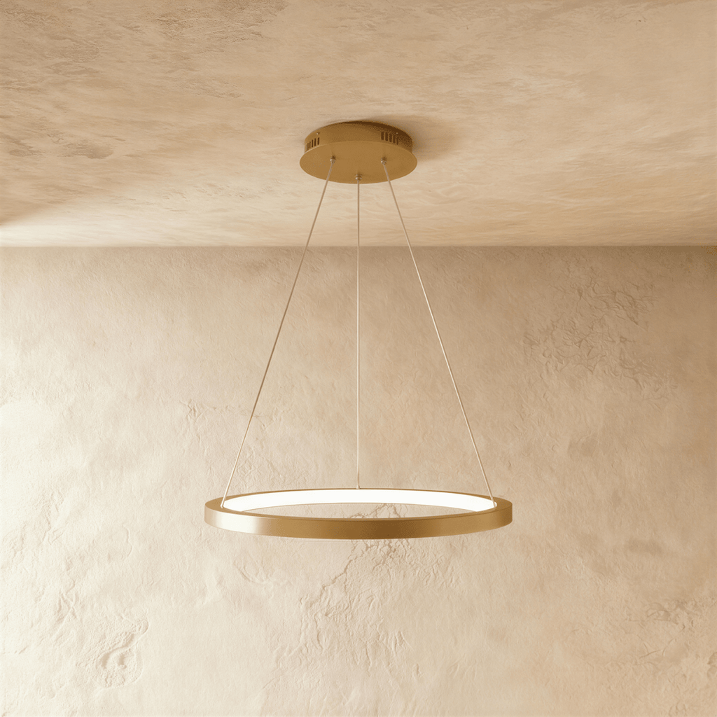 Clérachic's golden ring pendant floats gently, its LED edge glowing warm against a pale plaster backdrop.